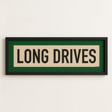 Framed sign with 'LONG DRIVES' text on a white wall