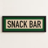 Framed sign with 'SNACK BAR' text on a white wall