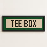Framed sign with 'TEE BOX' text on a white wall
