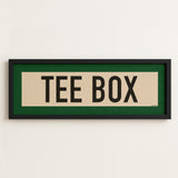 Framed sign with 'TEE BOX' text on a white wall
