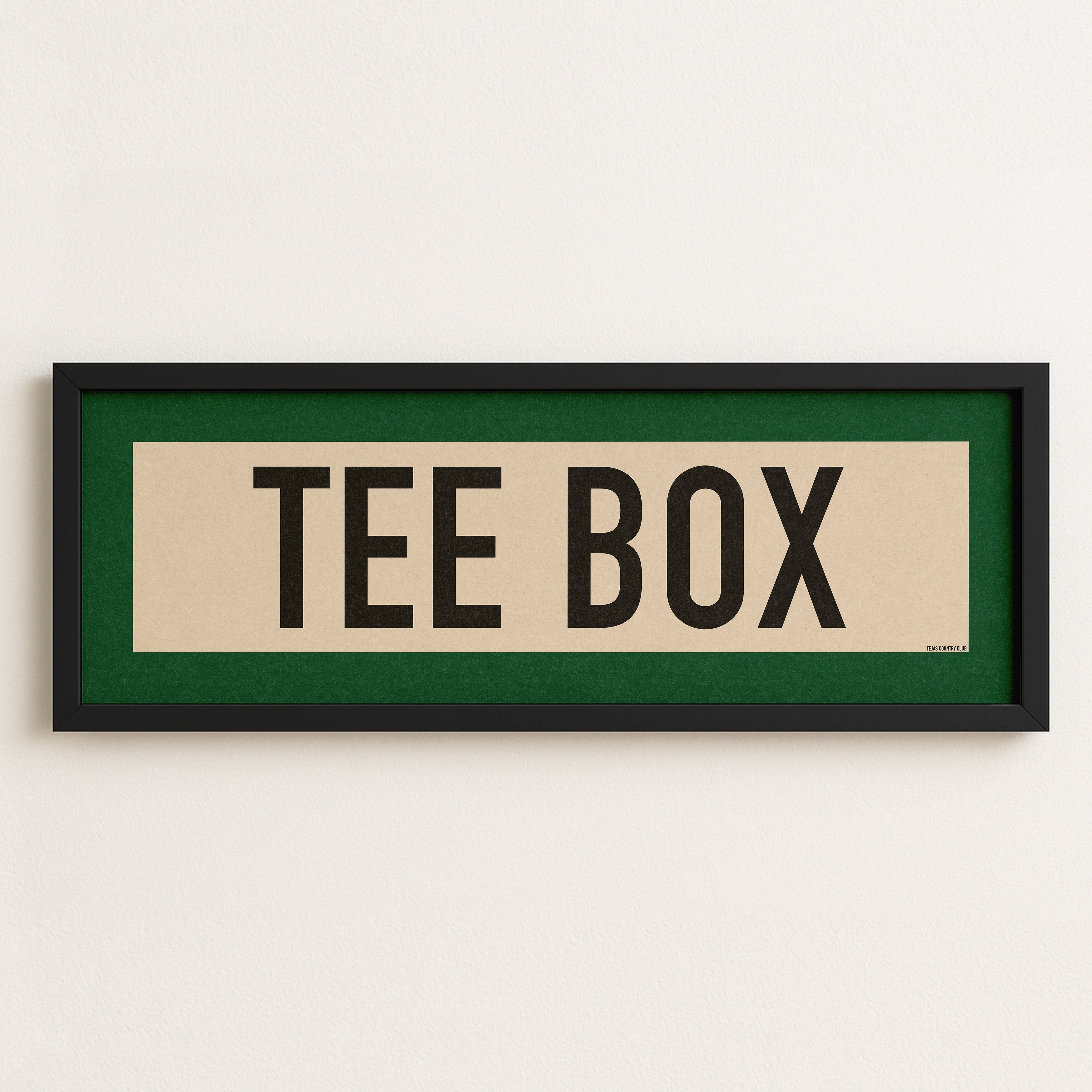 Framed sign with 'TEE BOX' text on a white wall
